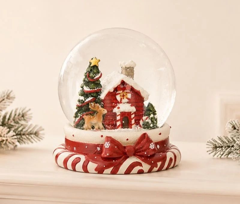 Boule à neige poly verre maison rouge enneigée sapins étoile dorée renne socle sucres orge nœud rouge Noël H11cm
