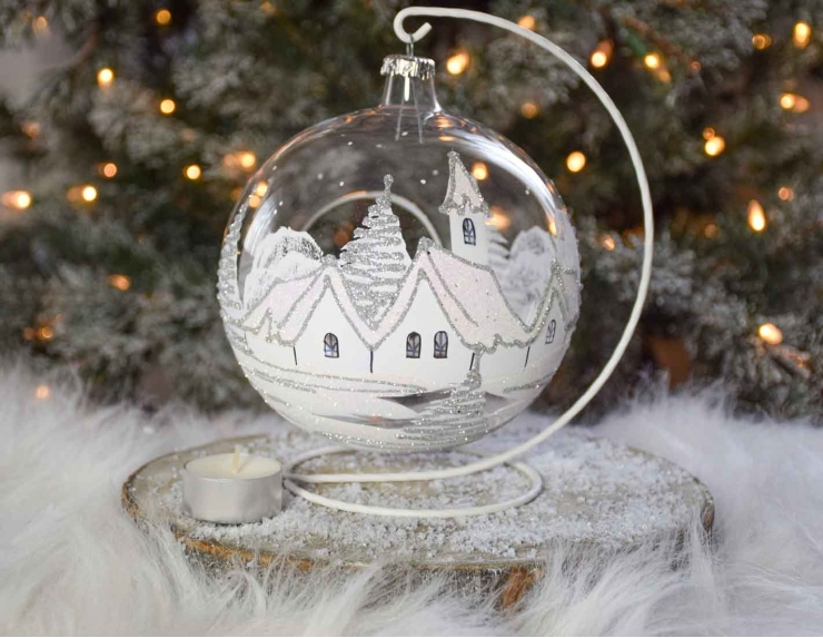 Grande boule bougeoir de Noël en verre soufflé avec un décor village blanc et paillettes argentées. Diamètre 15cm.
