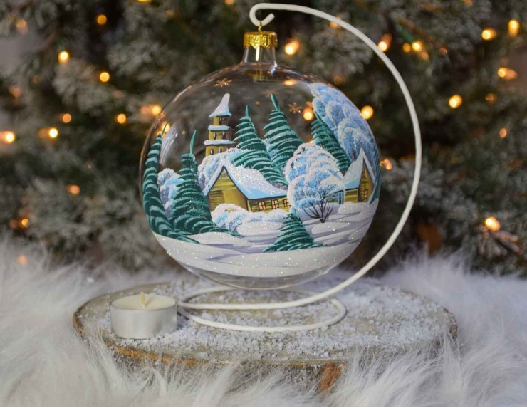 Grande boule bougeoir de Noël avec un chalet sous la neige entouré de sapins verts.Diamètre 15cm. Support blanc inclus.