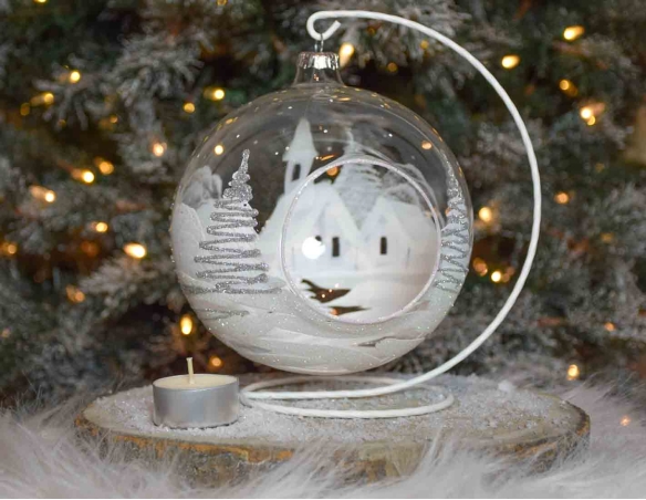 Grande boule bougeoir de Noël en verre soufflé avec un décor village blanc et paillettes argentées. Diamètre 15cm.