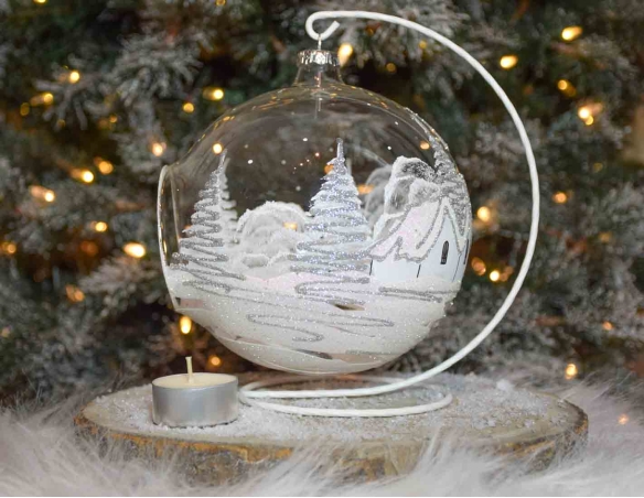Grande boule bougeoir de Noël en verre soufflé avec un décor village blanc et paillettes argentées. Diamètre 15cm.