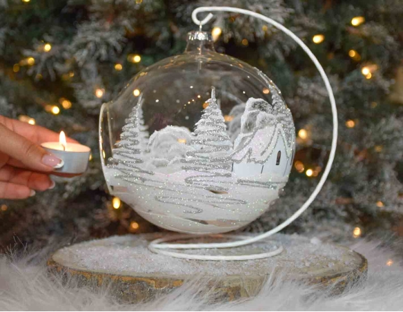 Grande boule bougeoir de Noël en verre soufflé avec un décor village blanc et paillettes argentées. Diamètre 15cm.