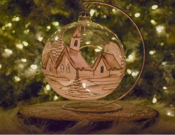Grande boule bougeoir de Noël en verre soufflé avec un décor village blanc et paillettes argentées. Diamètre 15cm.
