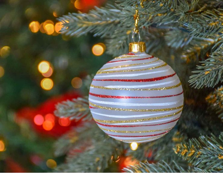 Boule de Noël blanche en verre recouverte de paillettes dorées, rouges et blanche en spirale tout autour de la boule.