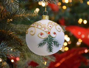 Boule de Noël blanche translucide avec décors de Noël traditionnel dorés et branches vertes.