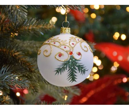 Boule de Noël blanche translucide avec décors de Noël traditionnel dorés et branches vertes.
