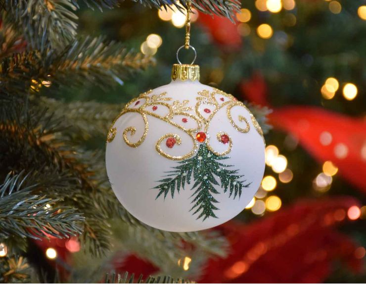 Boule de Noël blanche translucide avec décors de Noël traditionnel dorés et branches vertes.