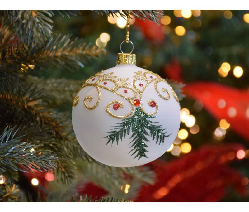 Boule de Noël blanche translucide avec décors de Noël traditionnel dorés et branches vertes.