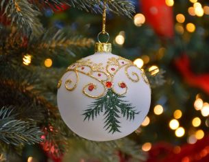 Boule de Noël blanche translucide avec décors de Noël traditionnel dorés et branches vertes.