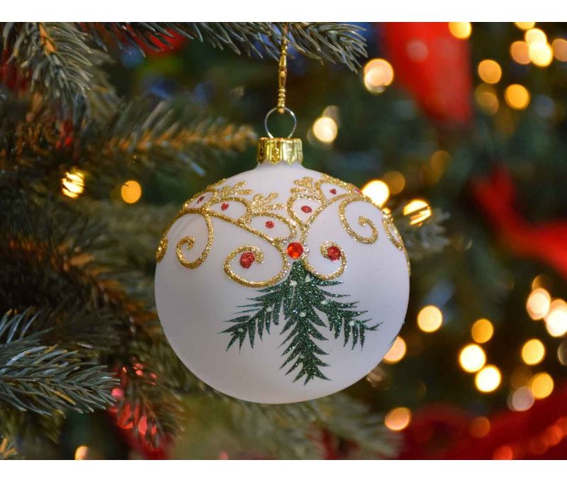 Boule de Noël blanche translucide avec décors de Noël traditionnel dorés et branches vertes.